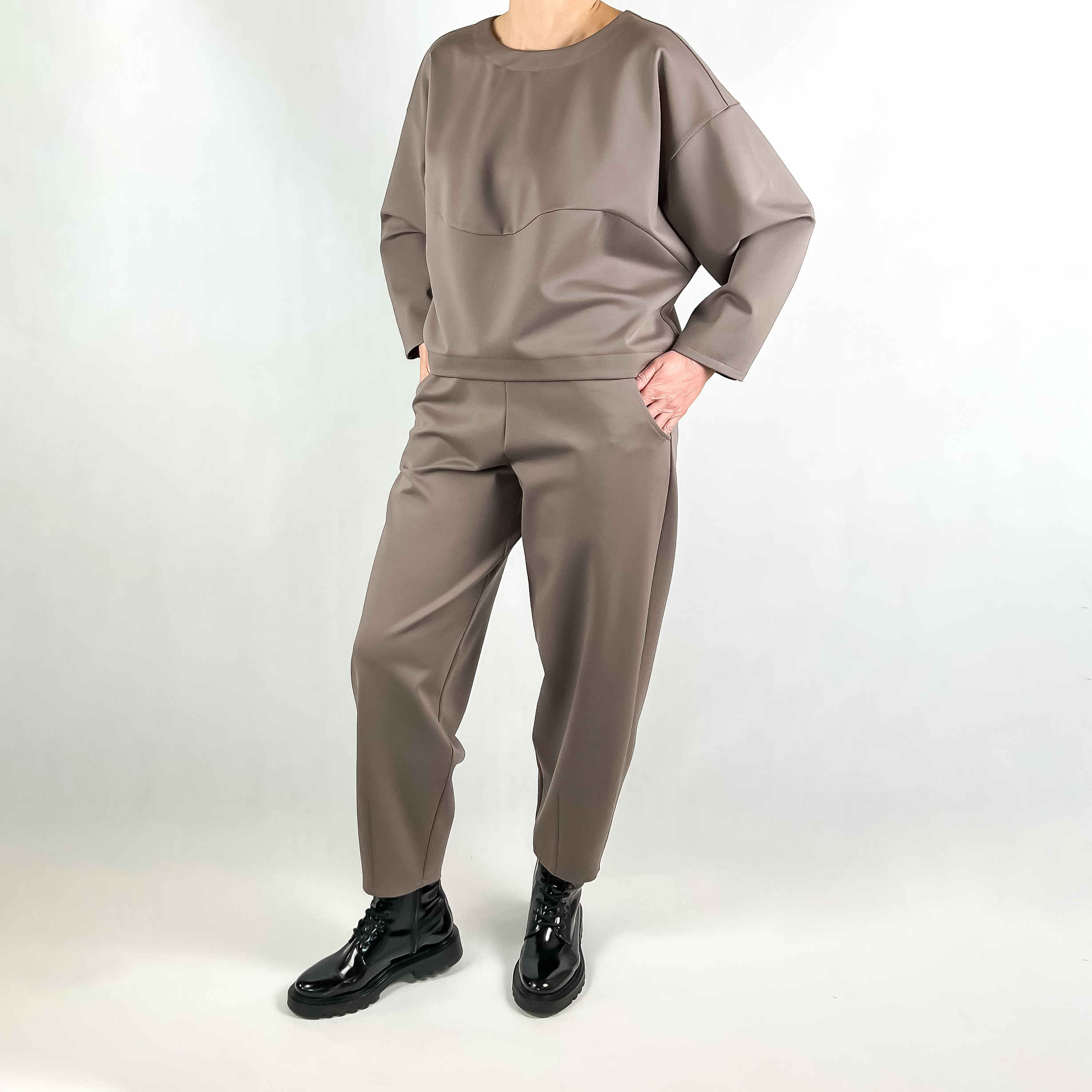 Moteris su banankio tipo kelnėmis „Latte“ stovinti prieš šviesų foną